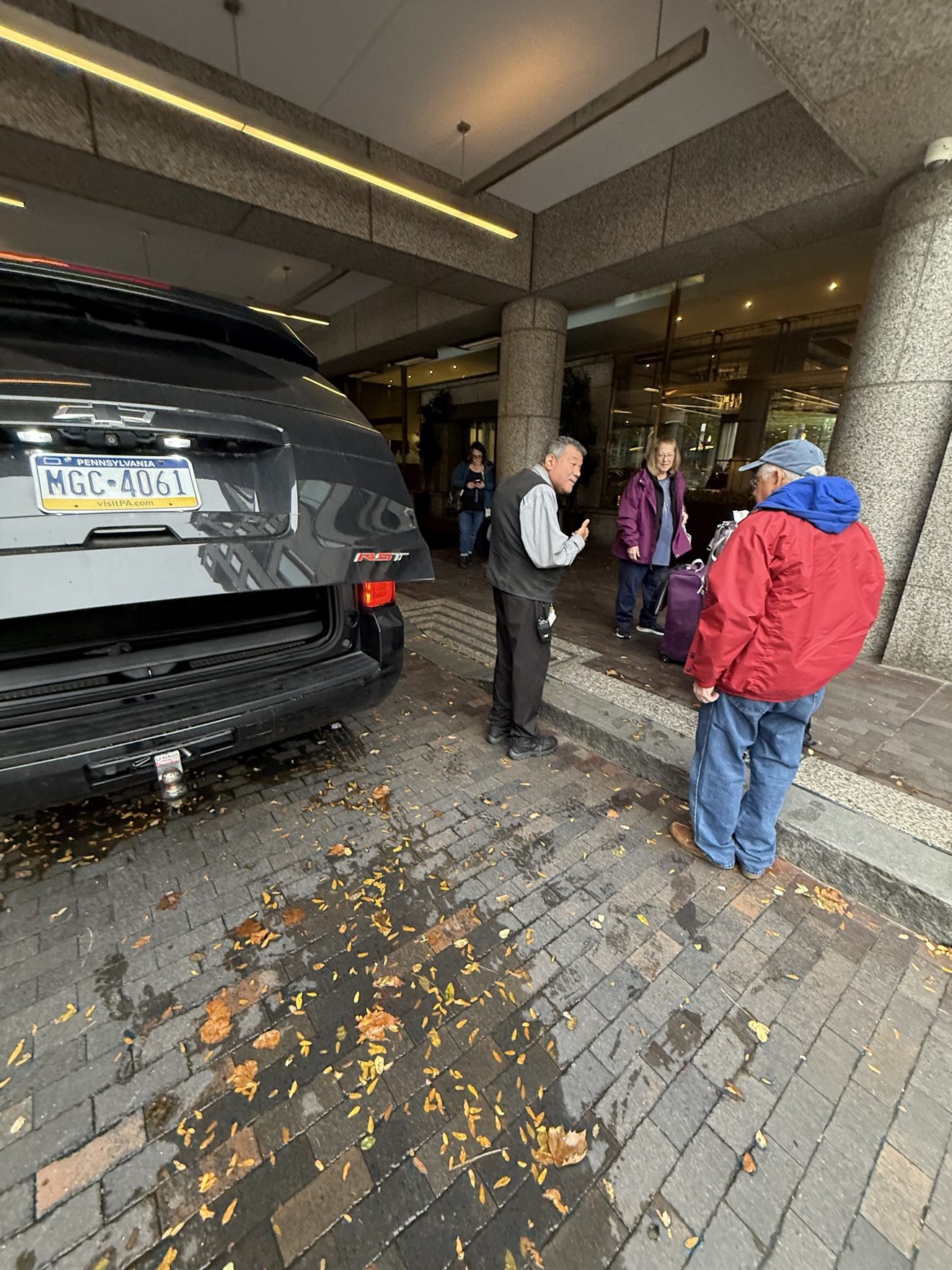 Chauffeur assisting hotel guests with luggage beside a black SUV